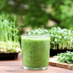 Green vegetable smoothie against background of greenery and microgreen. Healthy, vegan food, dieting concept. Selective focus.